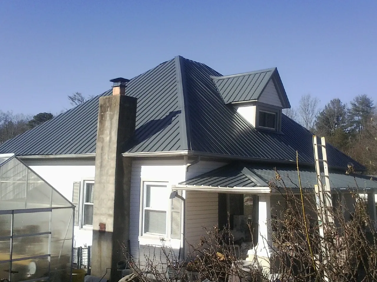 Dark blue standing seam metal roof on a white farmhouse with dormer — Slate & Tile Roof Repair by Roofing Brothers in Clear Brook