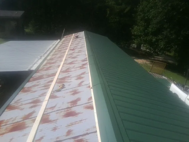 Old rusted panels beside newly installed green metal roofing — Wind Damage Roof Repair by Roofing Brothers in Clear Brook