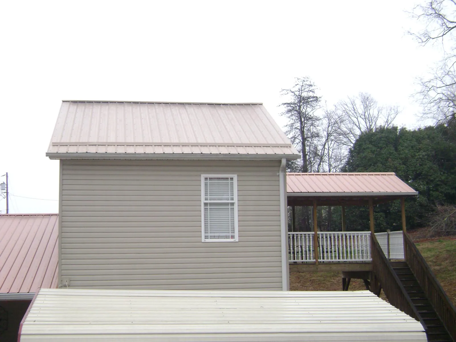 Tan metal roofs on a two story addition and attached porch, from a Roof Replacement job in Clear Brook